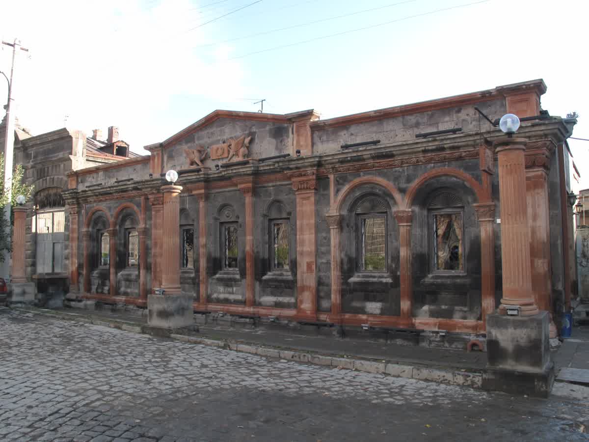 A historic Gyumri building showing the two-tone tuf stone construction, dark volcanic grey walls with contrasting warm reddish-orange stone pilasters and arched window frames